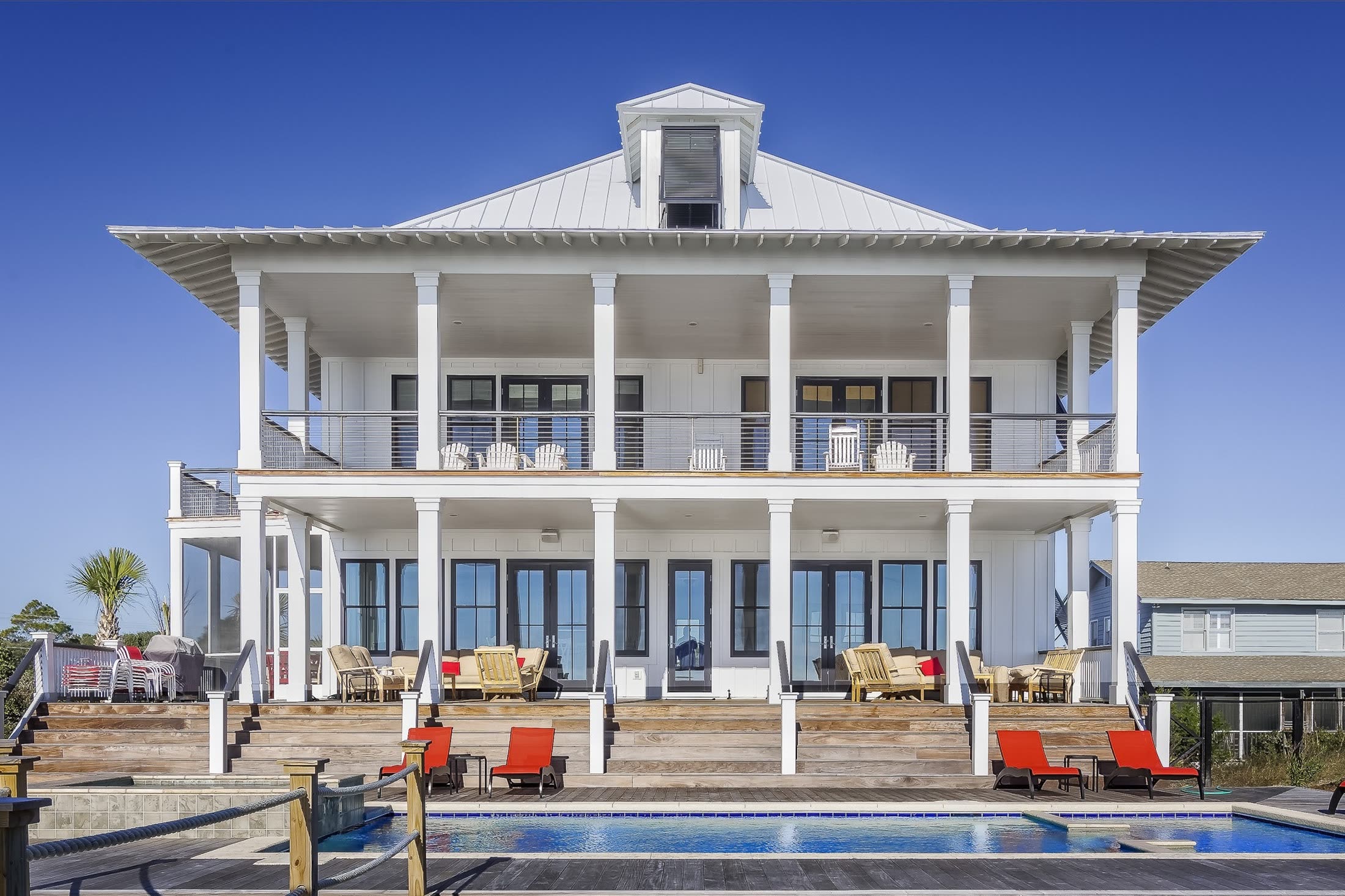 A white two-storey beach house with deep porches above a pool
